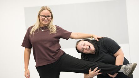 Zwei Lehrlinge sind zu sehen, die sich amüsieren. Die eine Person hält das Bein der anderen Person.