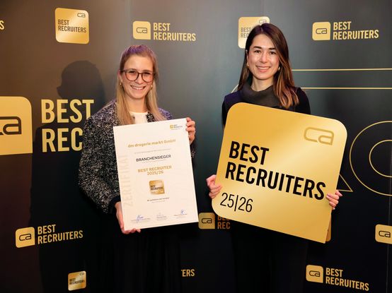 Zwei Frauen lächeln, halten einen Preis und ein Zertifikat und stehen vor einem Hintergrund mit der Aufschrift Beste Recruiter