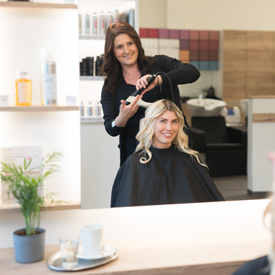 Friseurin macht einer Kundin Locken. Im Hintergrund ist das dm friseurstudio sichtbar.