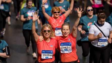 Mitarbeiterinnen in dm gebrandeten Shirts halten die Hände hoch und lächeln in die Kamera. Umgeben sind die Frauen von anderen Läuferinnen beim Frauanlauf.