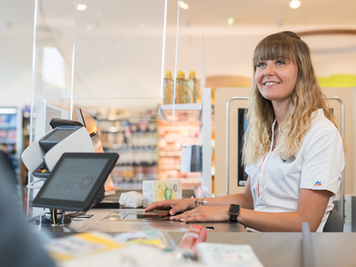 Eine Mitarbeiterin an der Kasse im dm Markt scannt Produkte eines Kunden und lächelt ihn dabei an.
