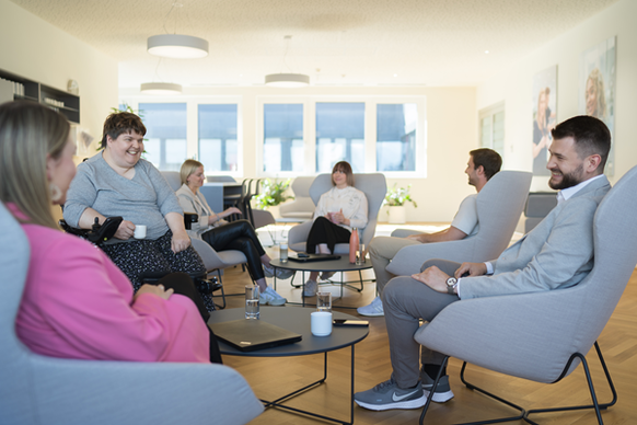 Mitarbeiterinnen und Mitarbeiter sitzen in Gruppen im Cafébereich und führen angeregte Gespräche. Die entspannte Atmosphäre lädt zum Austausch und zur Zusammenarbeit ein.