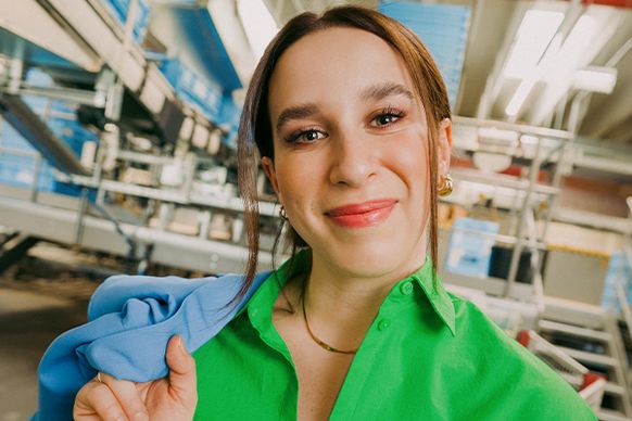 Eine Mitarbeiterin in einem hellgrünen Shirt lächelt und steht in einer modernen Lagerumgebung.