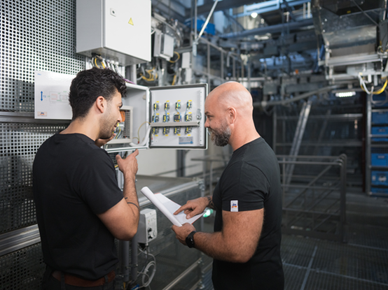 Zwei Mitarbeitende schauen sich den Stromkasten im Lager an und tauschen sich darüber aus.