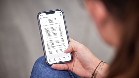 Auf einem Smartphone ist ein eBon zu sehen. Das Smartphone wird von einer Frau gehalten.