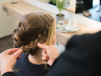 Friseurin flechtet einen Hochsteckfrisur bei einer Kundin und hält einen Kamm in der Hand.