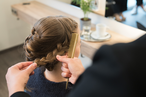 Friseurin flechtet einen Hochsteckfrisur bei einer Kundin und hält einen Kamm in der Hand.