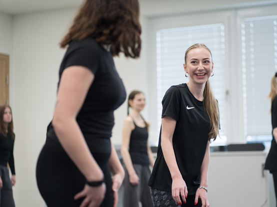 Eine Gruppe von Lehrlingen in sportlicher Kleidung bei einem Tanzworkshop in lockerer und dynamischen Athmosphäre.