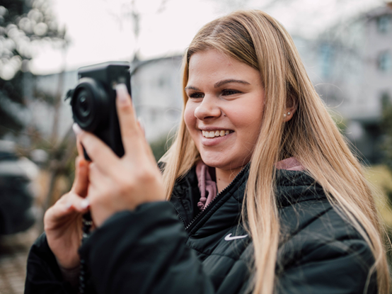 Ein Lehrling hält eine Kamera in der Hand und richtet sie auf ein Motiv.