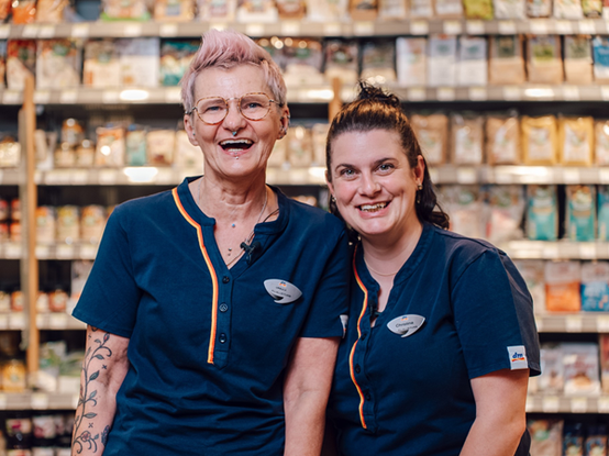 Ein Jobsharing Tandem steht vor einem Regal im dm Markt und lächeln in die Kamera.