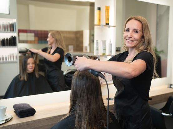 Eine Mitarbeiterin im dm kosmetikstudio lackiert die Nägel einer Kundin, die am Behandlungsstuhl sitzt. Beide wirken fröhliche und zufrieden.