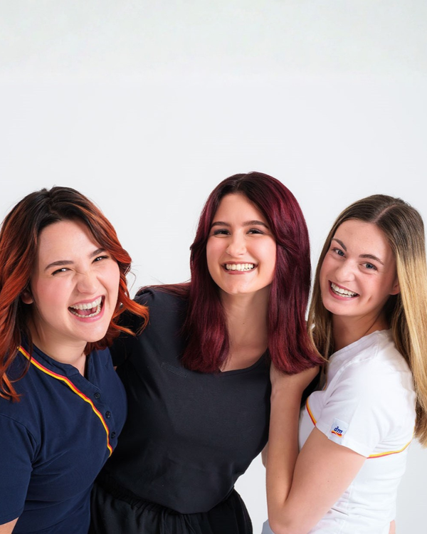 Drei Lehrlinge stehen zusammen und lächeln.